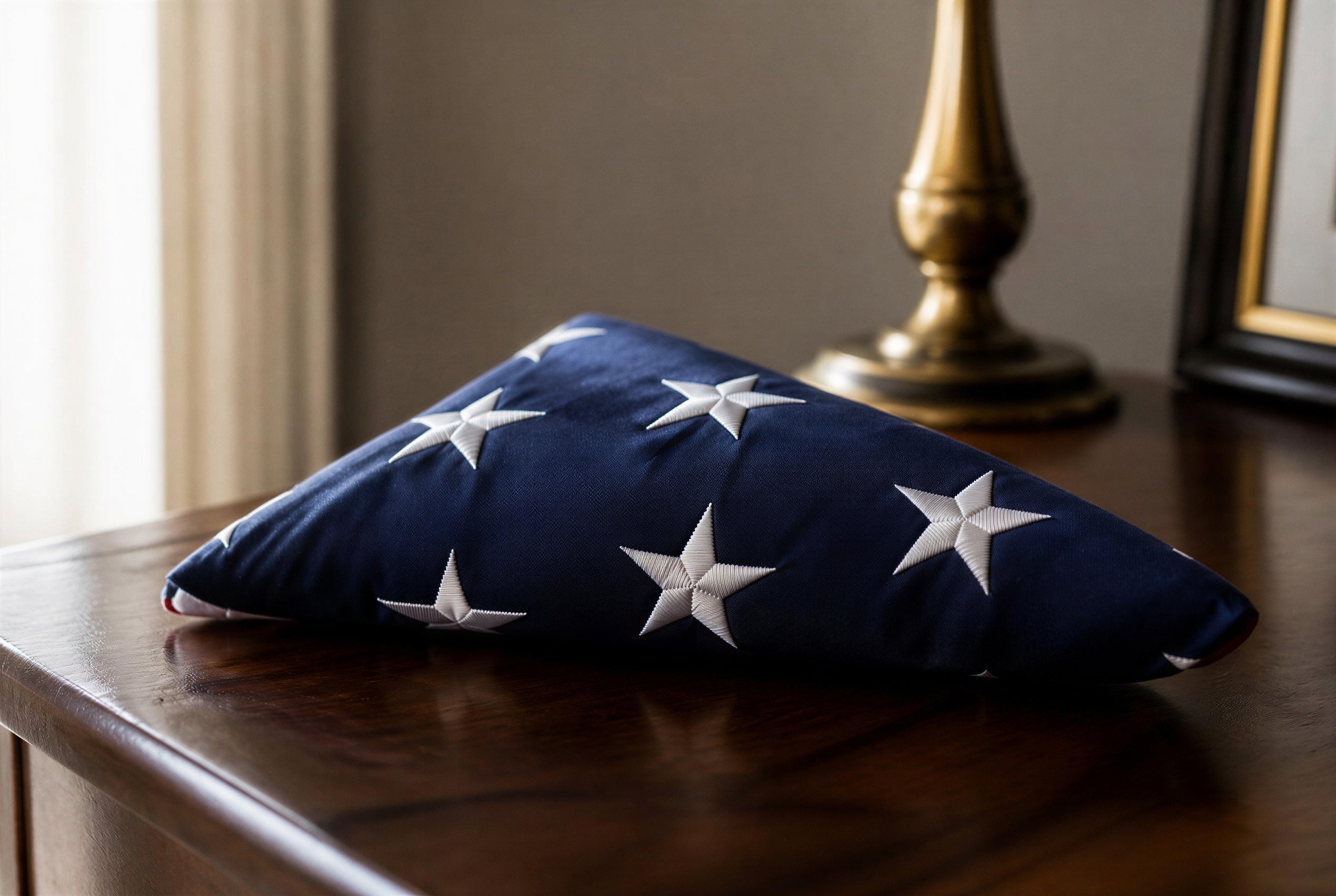 A folded American flag resting on a dark wooden surface, with a brass lamp and framed photo softly blurred in the background — a dignified image for a military veteran's funeral program guide.
