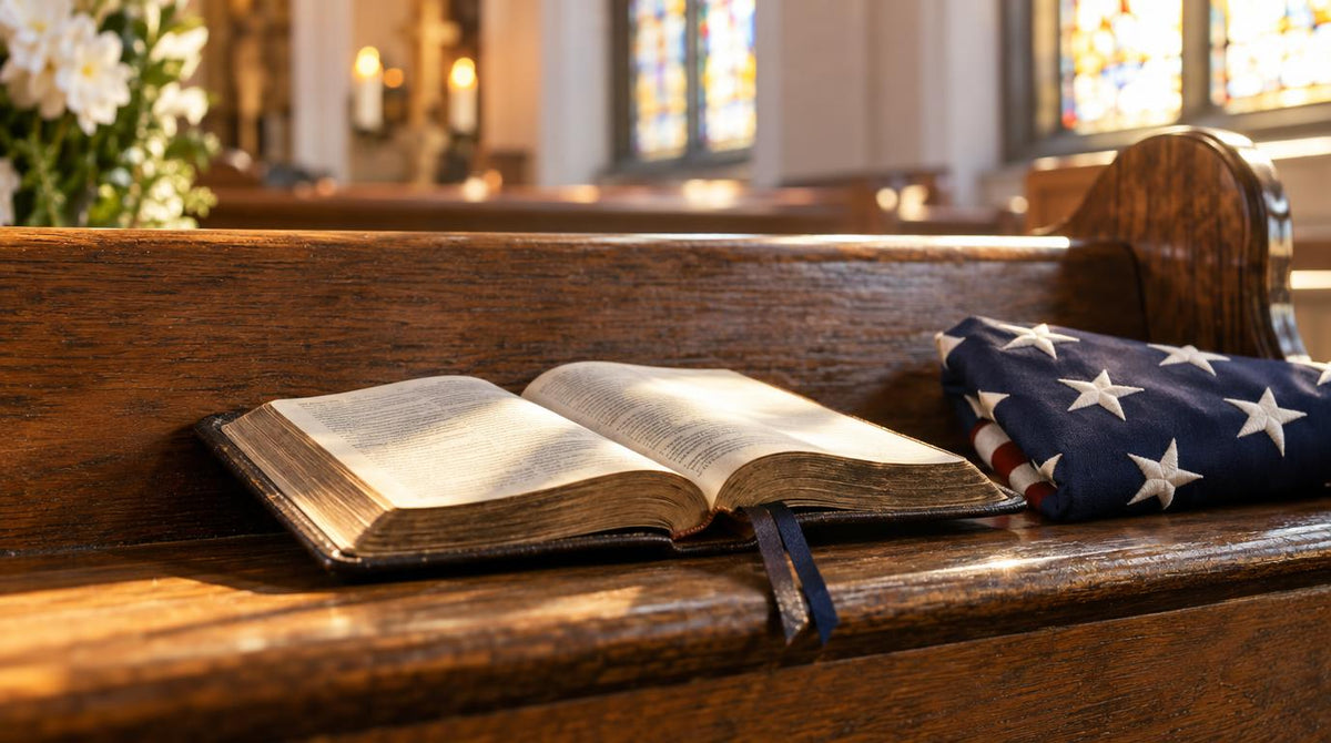 Open prayer book on a wooden church pew beside a folded American flag, with stained glass windows and white flowers in the background