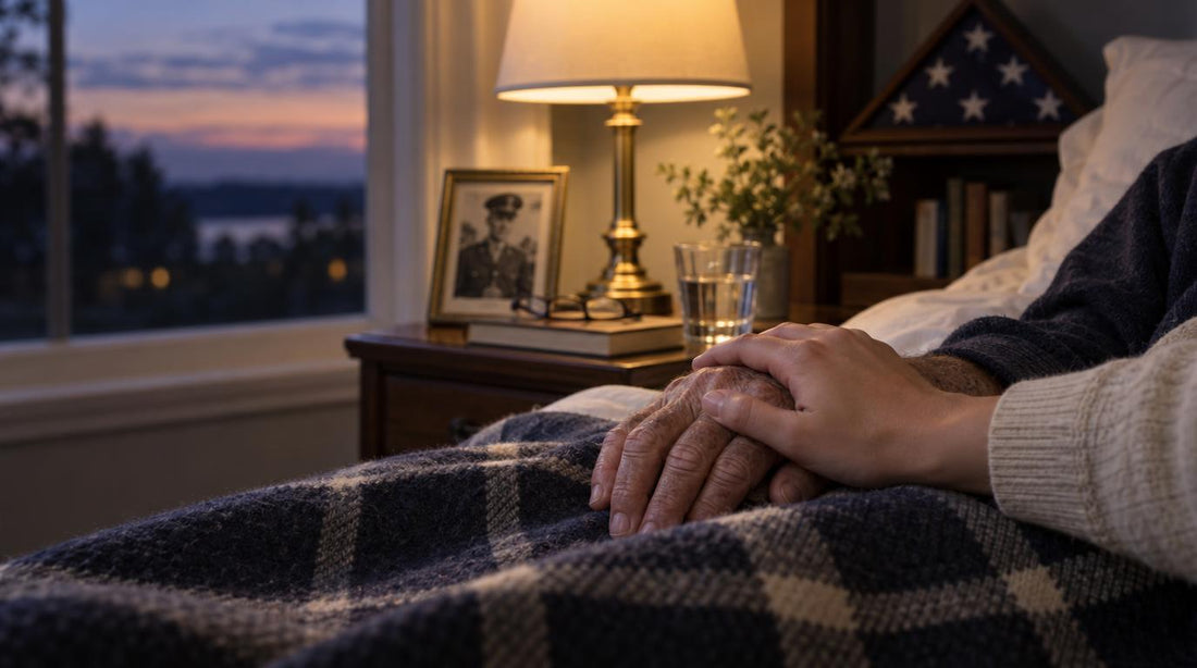A warm lamp on a bedside table beside an old photograph, with a younger hand gently holding an older one on a folded blanket.
