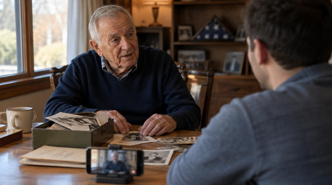 An older veteran shares stories at the kitchen table while a family member records on a phone, with old service photos and a folded flag nearby.