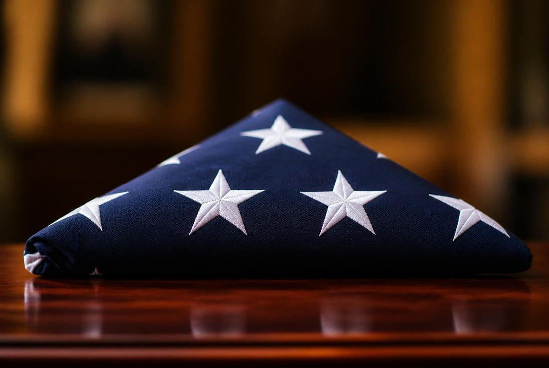 A neatly folded American flag resting on a polished wooden surface, its white stars visible against the deep navy blue field — header image for a guide to the flag at a military funeral