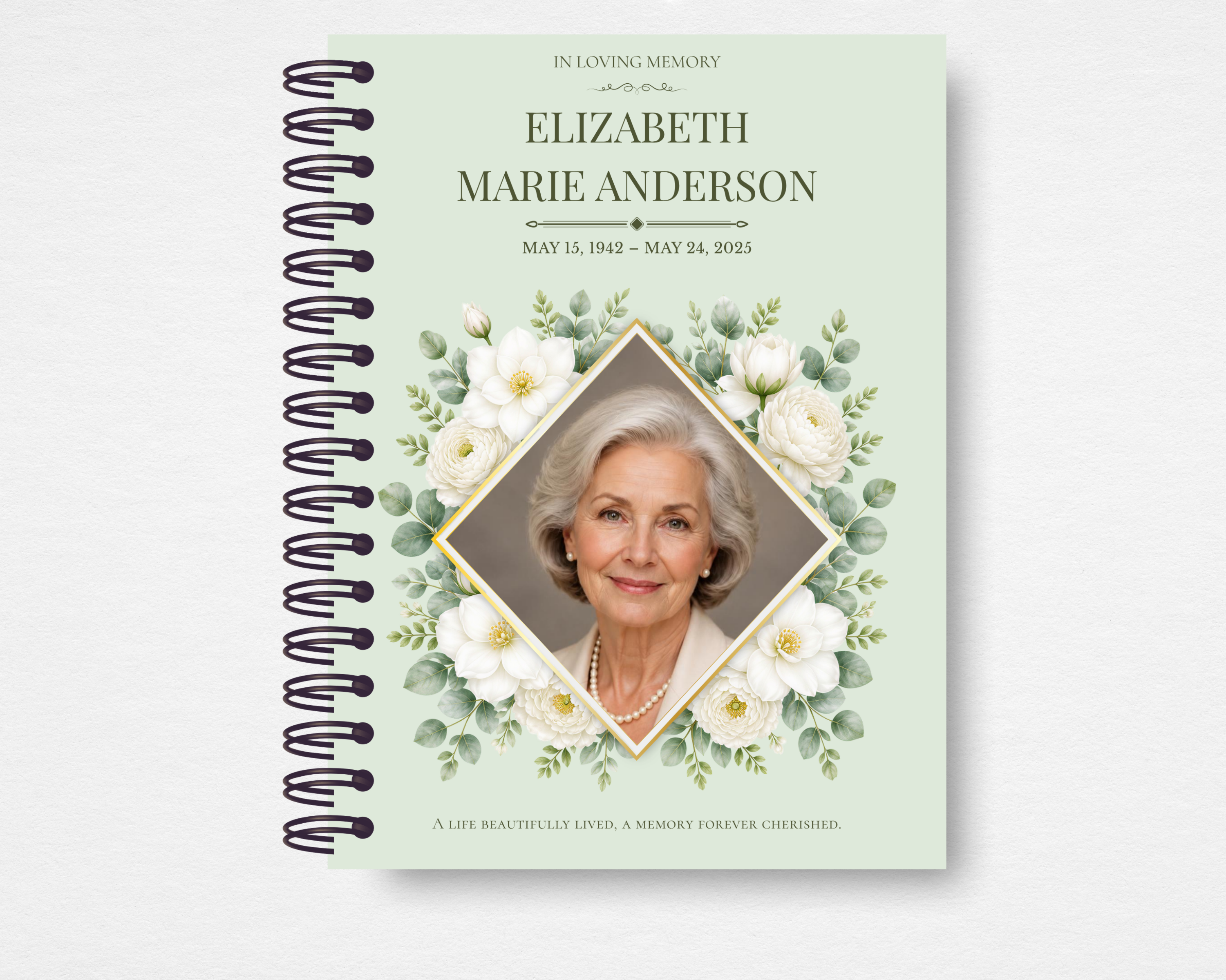 Product mockup of the Sage & Ivory memorial guest book — soft sage green cover with ivory gardenias and eucalyptus sprigs framing a gold diamond portrait frame, name and dates in dark serif type, and a sentiment line along the bottom edge.

